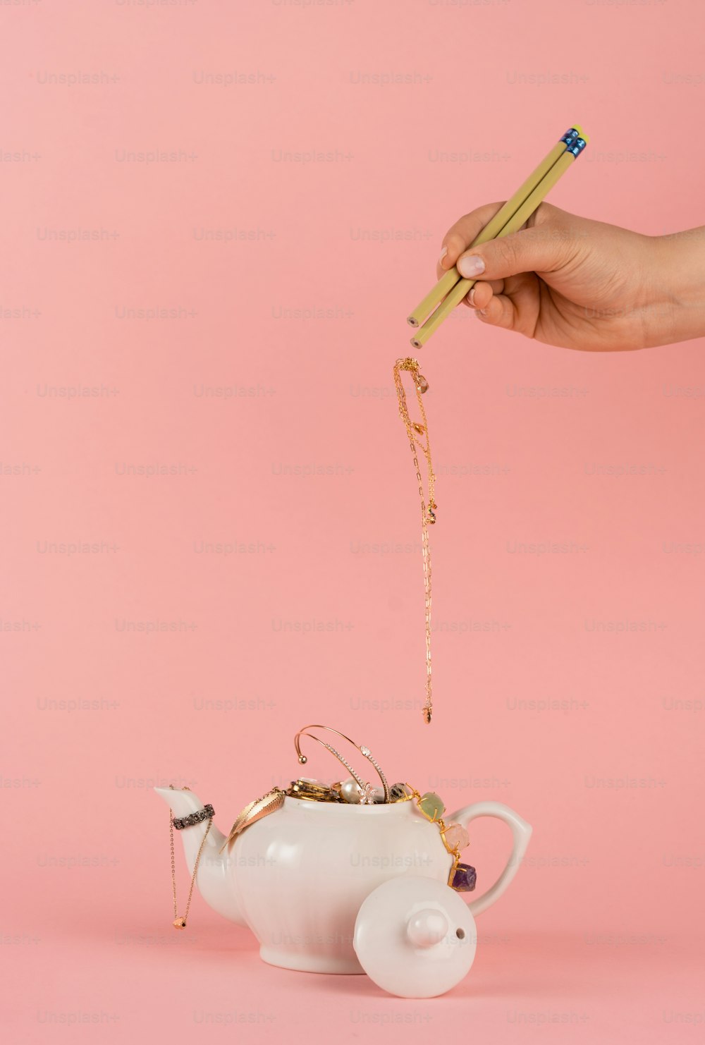 a person holding a pair of chopsticks above a teapot