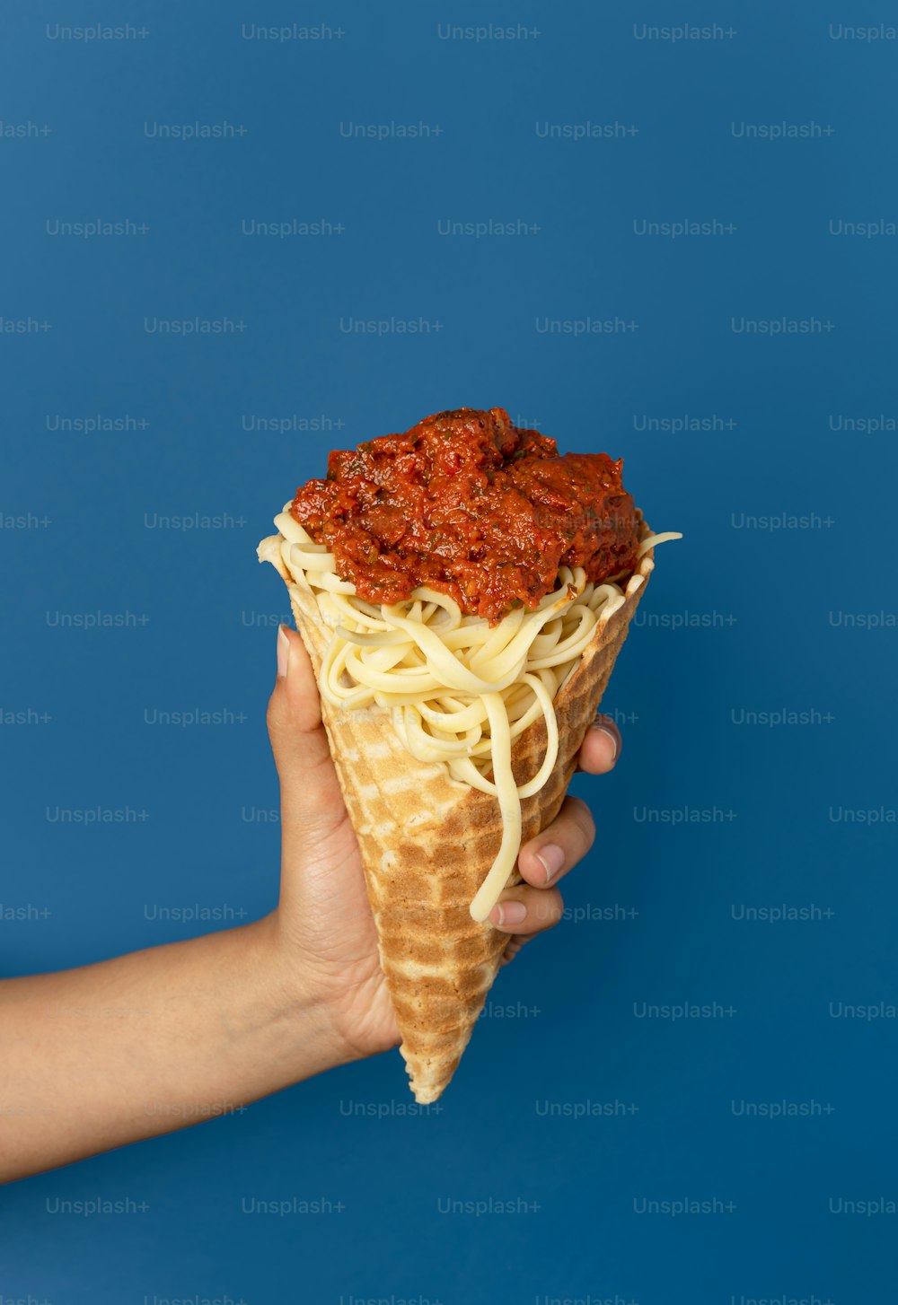 a hand holding a waffle filled with noodles and sauce