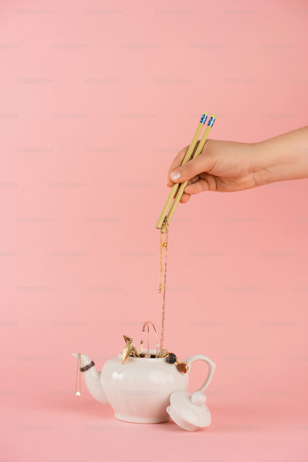a person holding a pair of chopsticks over a teapot