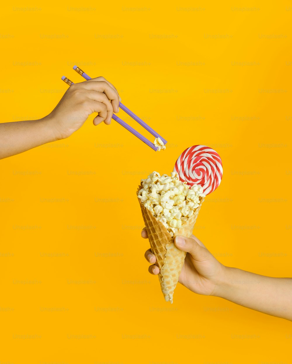 due mani che tengono un cono waffle pieno di popcorn e due lecca-lecca