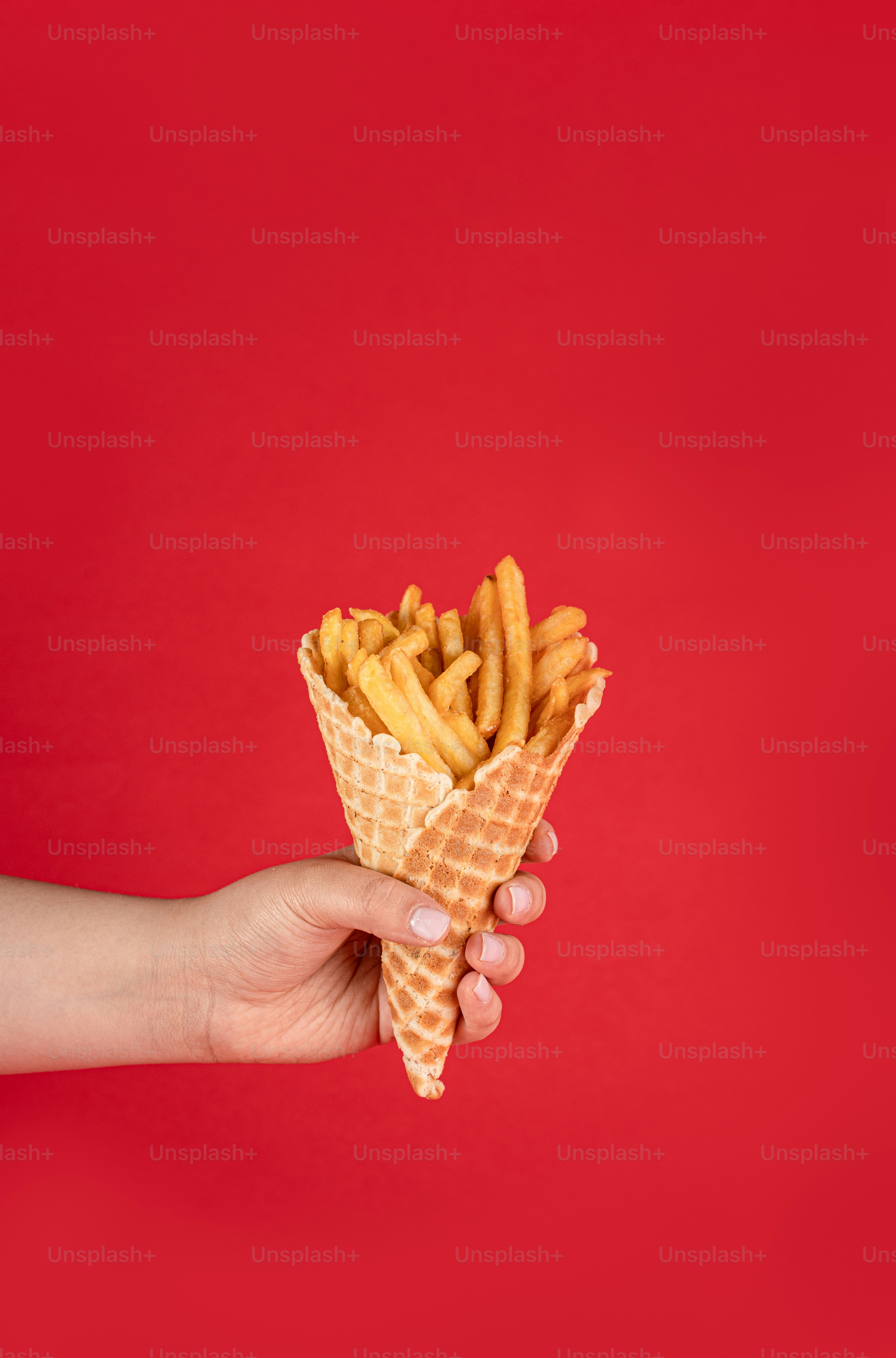 eine Hand, die eine mit Pommes Frites gefüllte Waffeltüte hält