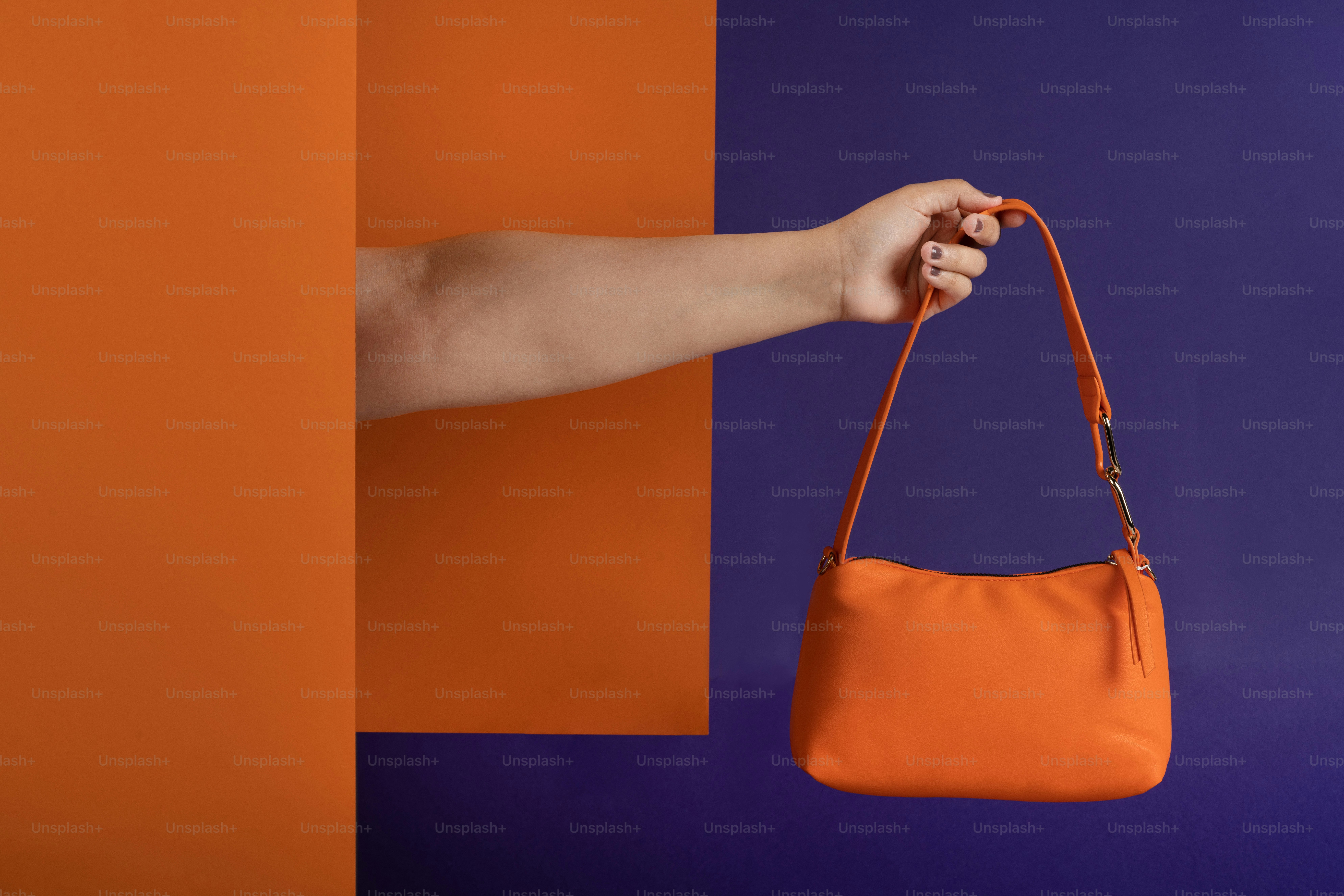 die hand einer frau, die eine orangefarbene handtasche hält