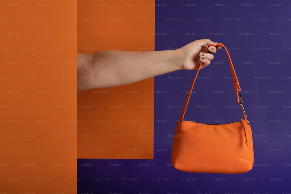 a woman's hand holding an orange purse