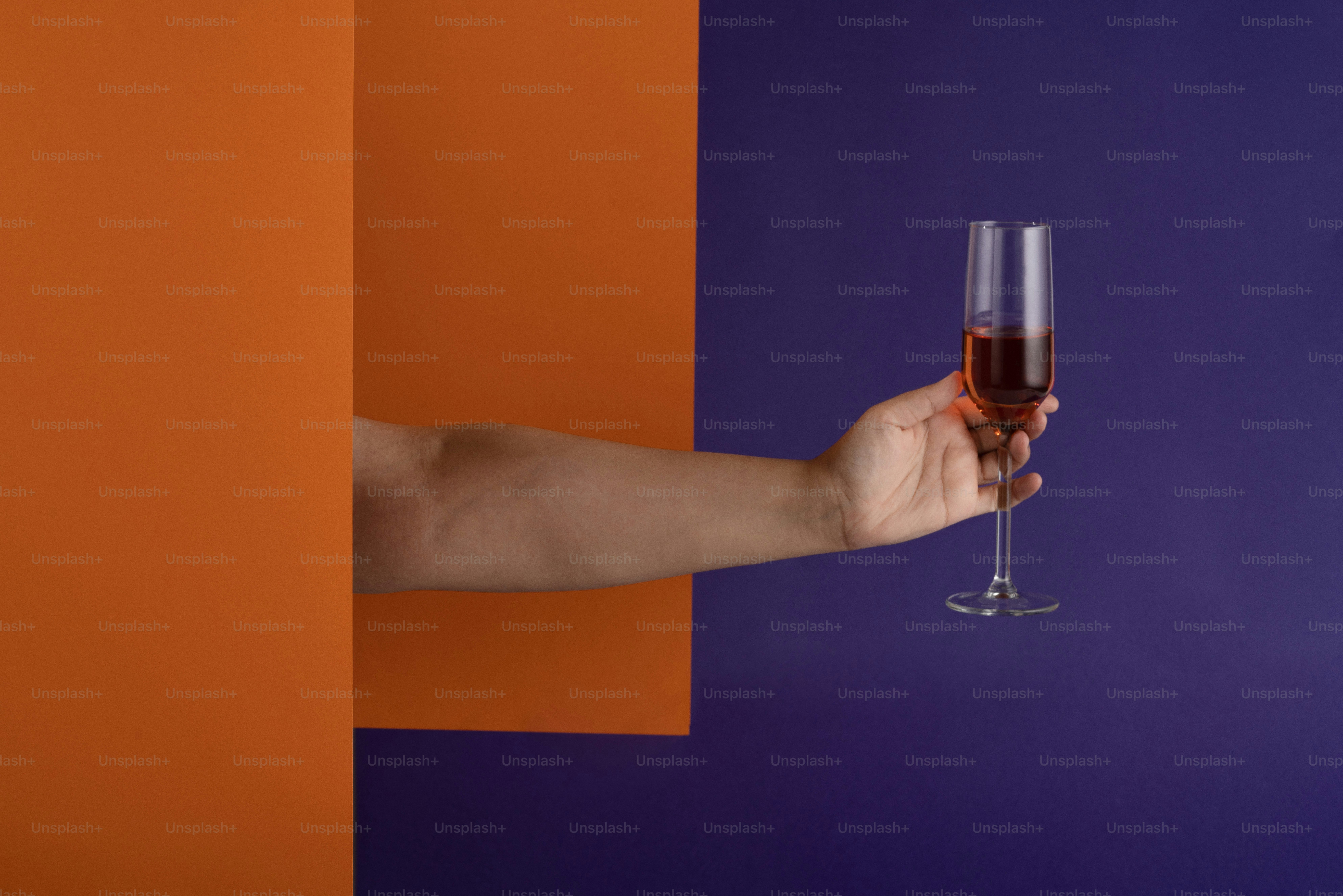 eine hand, die ein weinglas vor einer lila und orangefarbenen wand hält