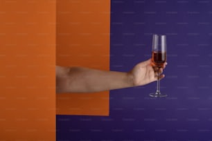 Una mano sosteniendo una copa de vino frente a una pared púrpura y naranja