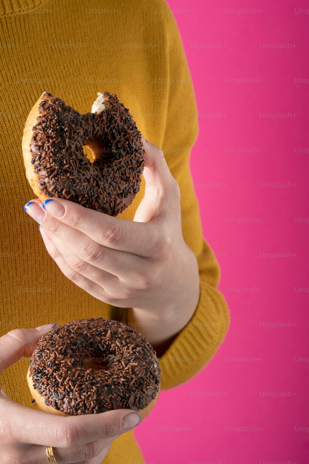 a woman holding a chocolate donut with sprinkles