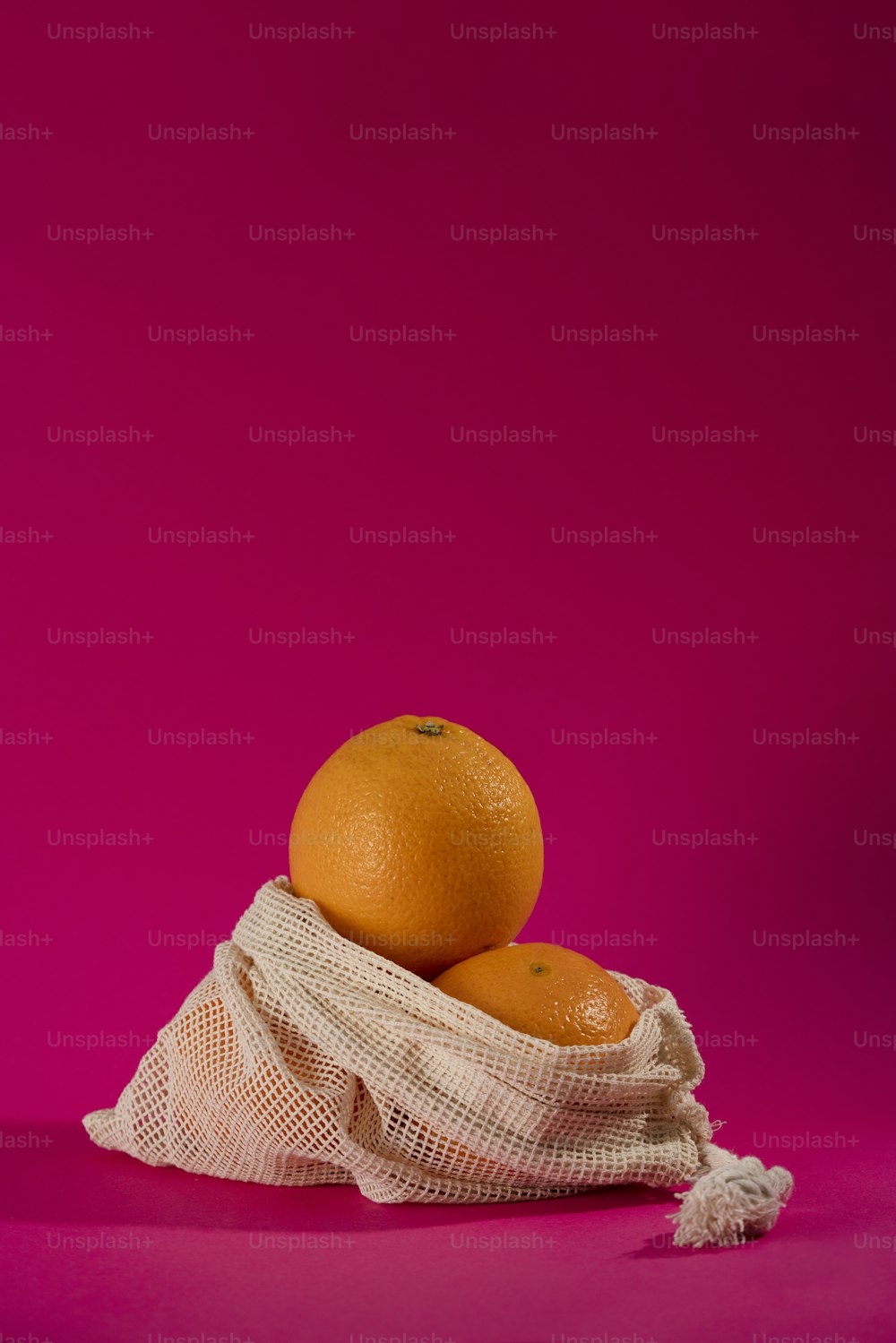 two oranges in a mesh bag on a pink background