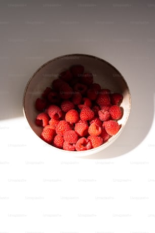 a bowl of raspberries on a white surface