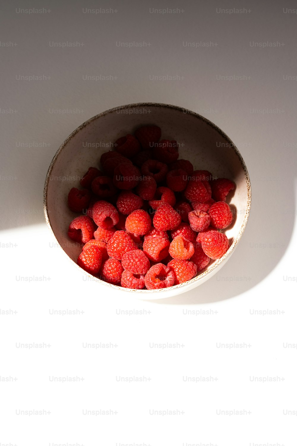 a bowl of raspberries on a white surface