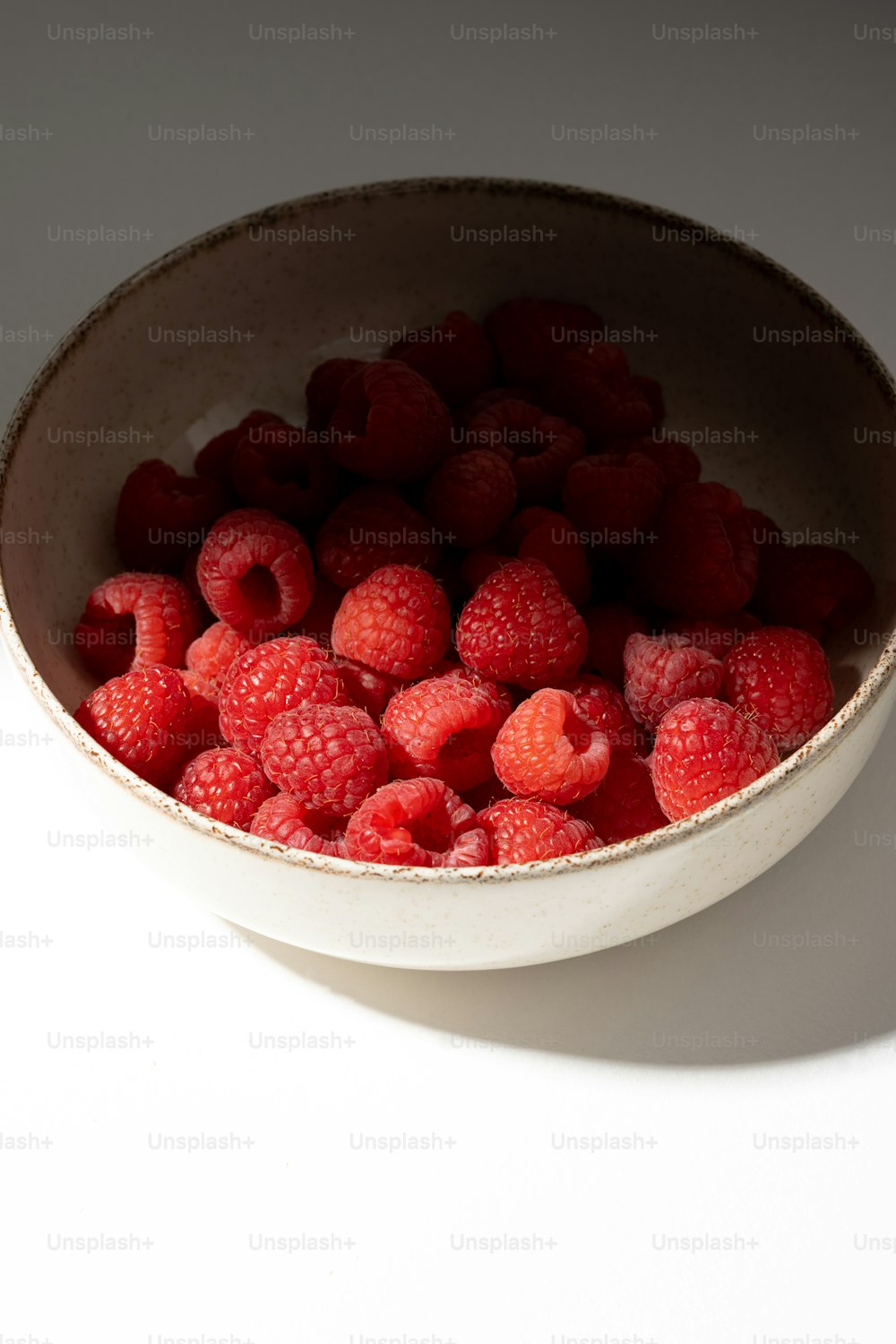 a white bowl filled with raspberries on top of a table