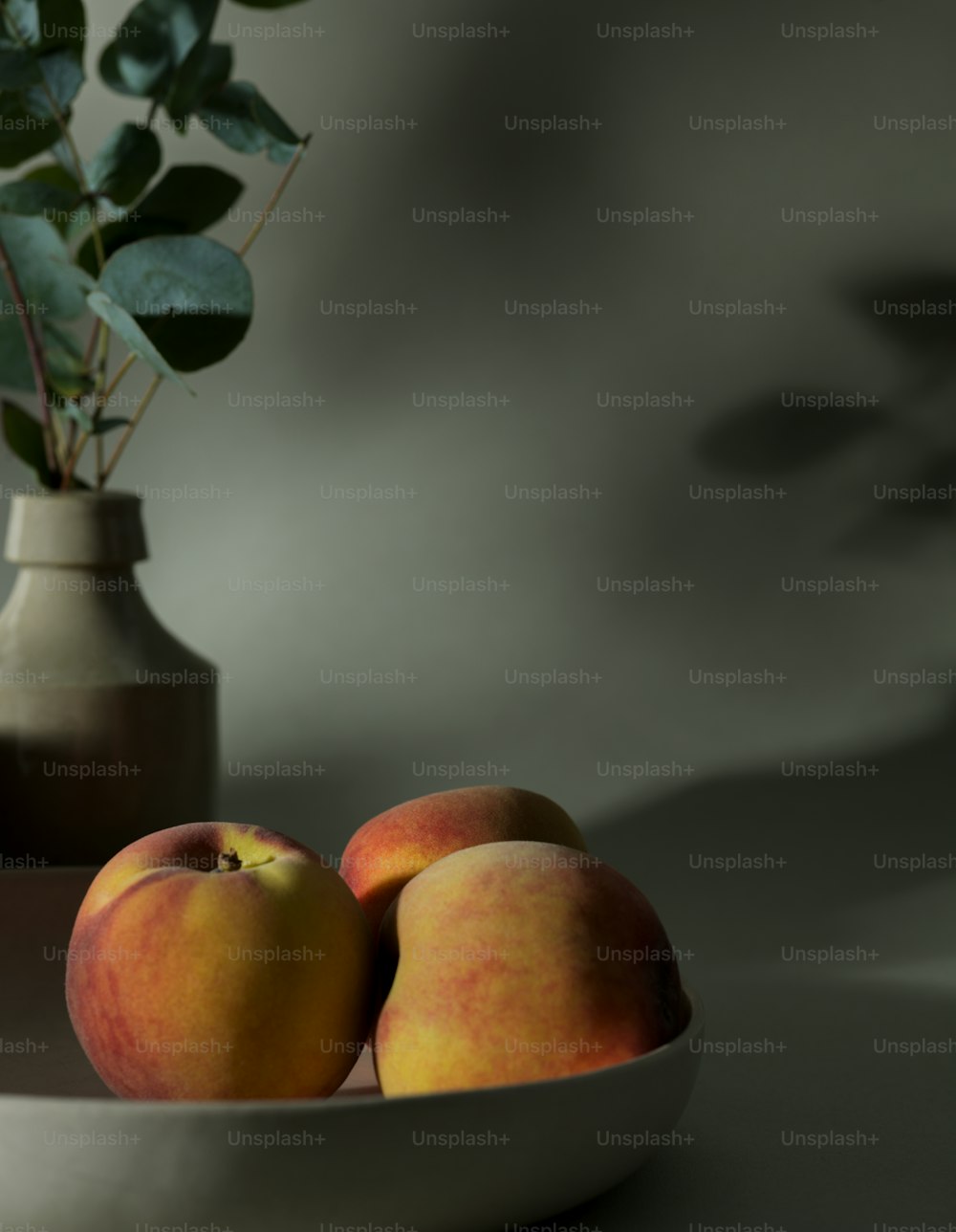 ein weißer Teller mit drei Pfirsichen neben einer Vase