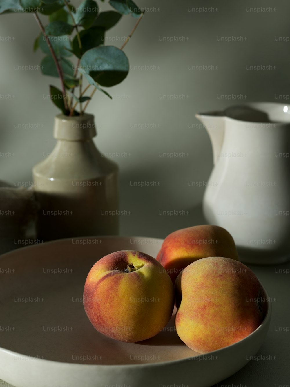 two peaches on a plate next to a vase of flowers