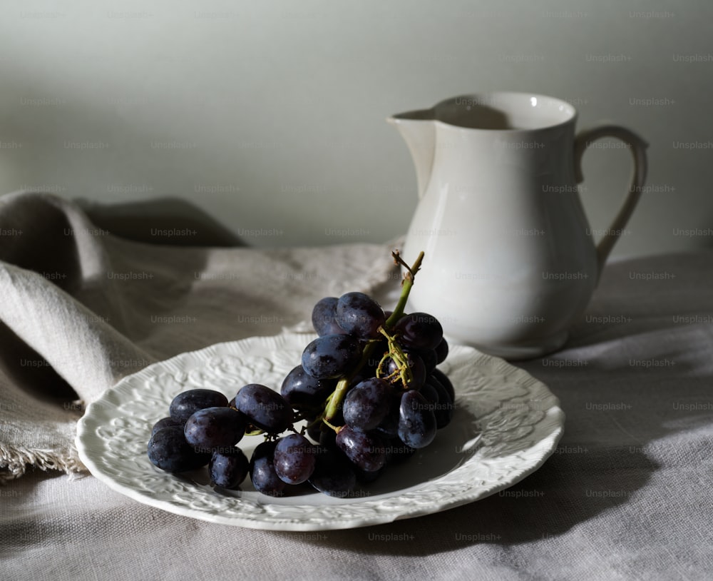a plate with grapes on it next to a pitcher