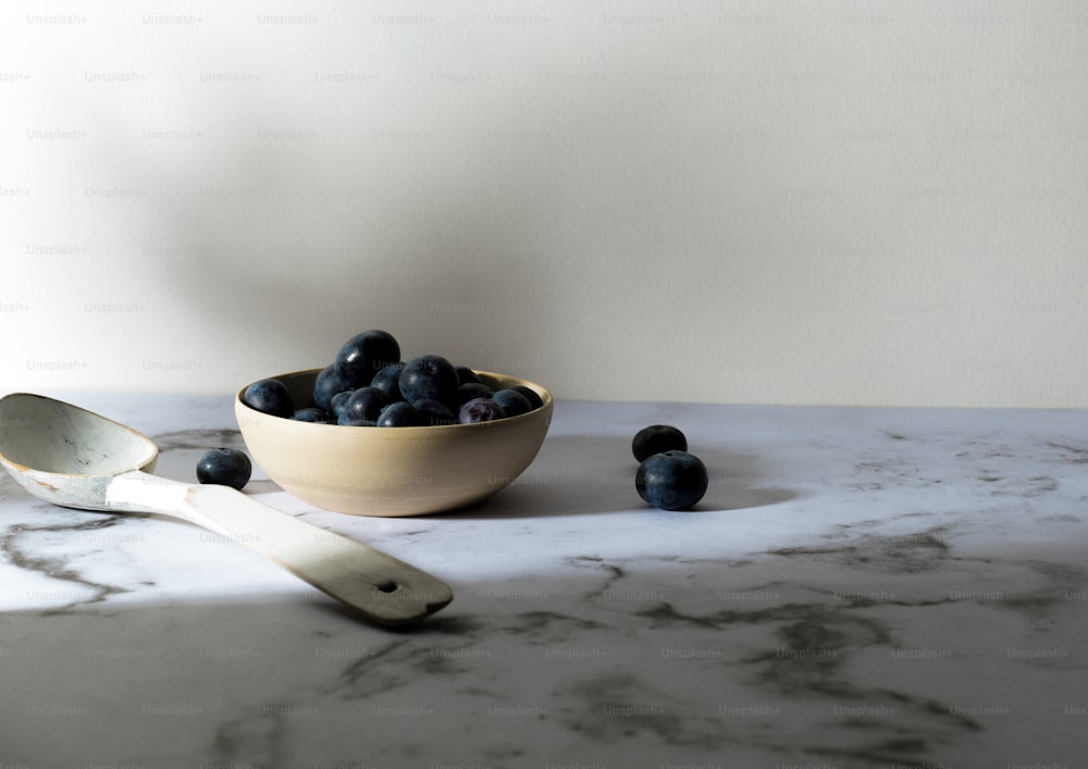 a bowl of blueberries and a spoon on a marble counter