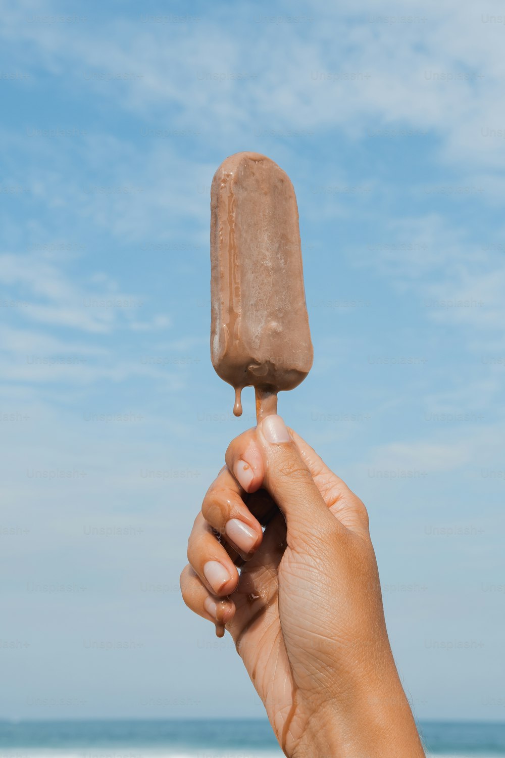 una mano sosteniendo un helado de chocolate en un palo