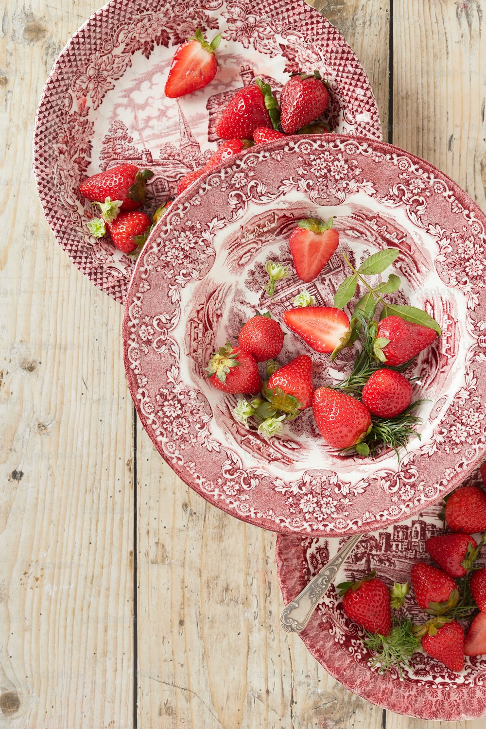 drei Teller mit Erdbeeren darauf auf einem Holztisch
