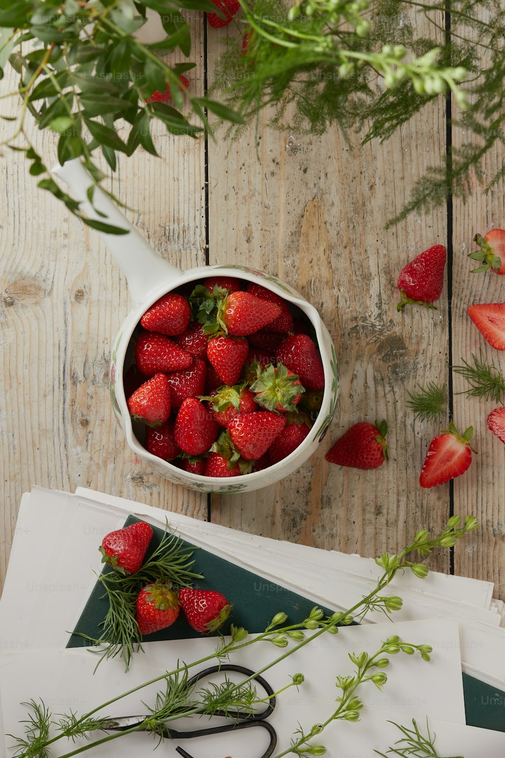 a bowl of strawberries on a table with a pair of scissors