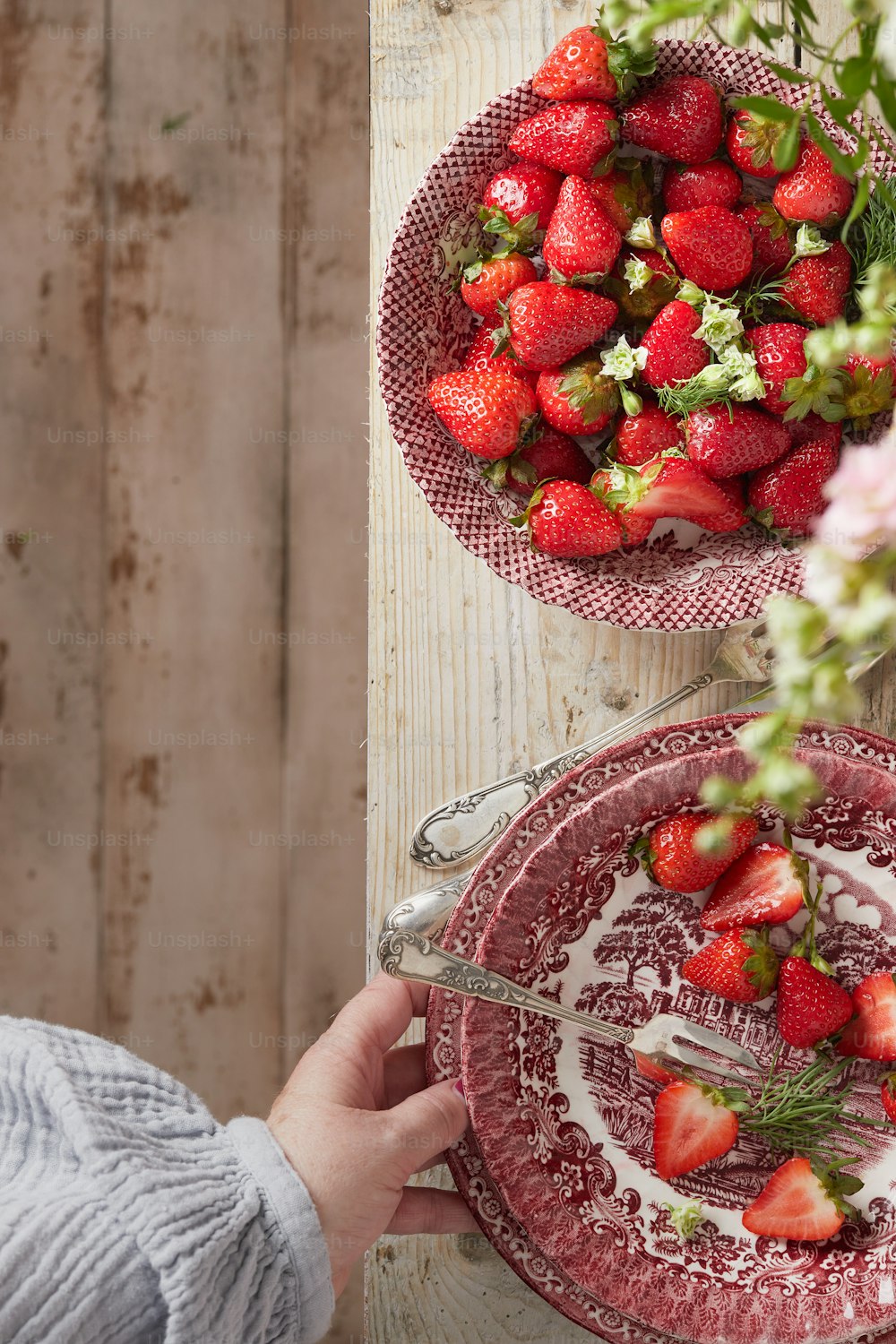 a plate of strawberries with a bowl of strawberries in the background