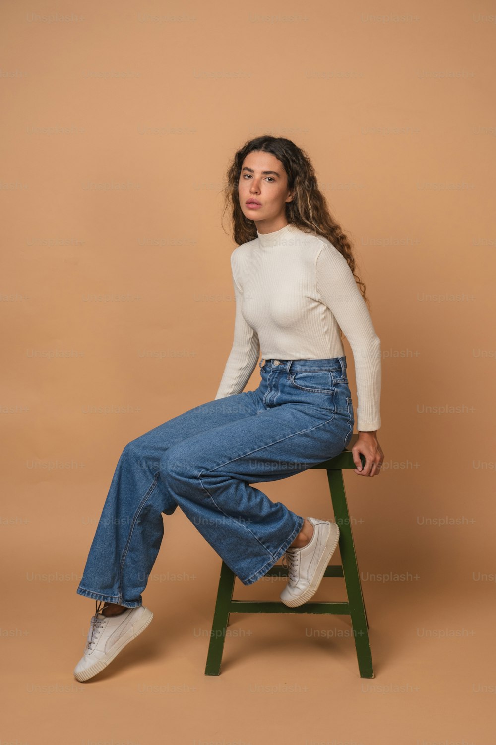 a woman sitting on a stool wearing a white top and jeans