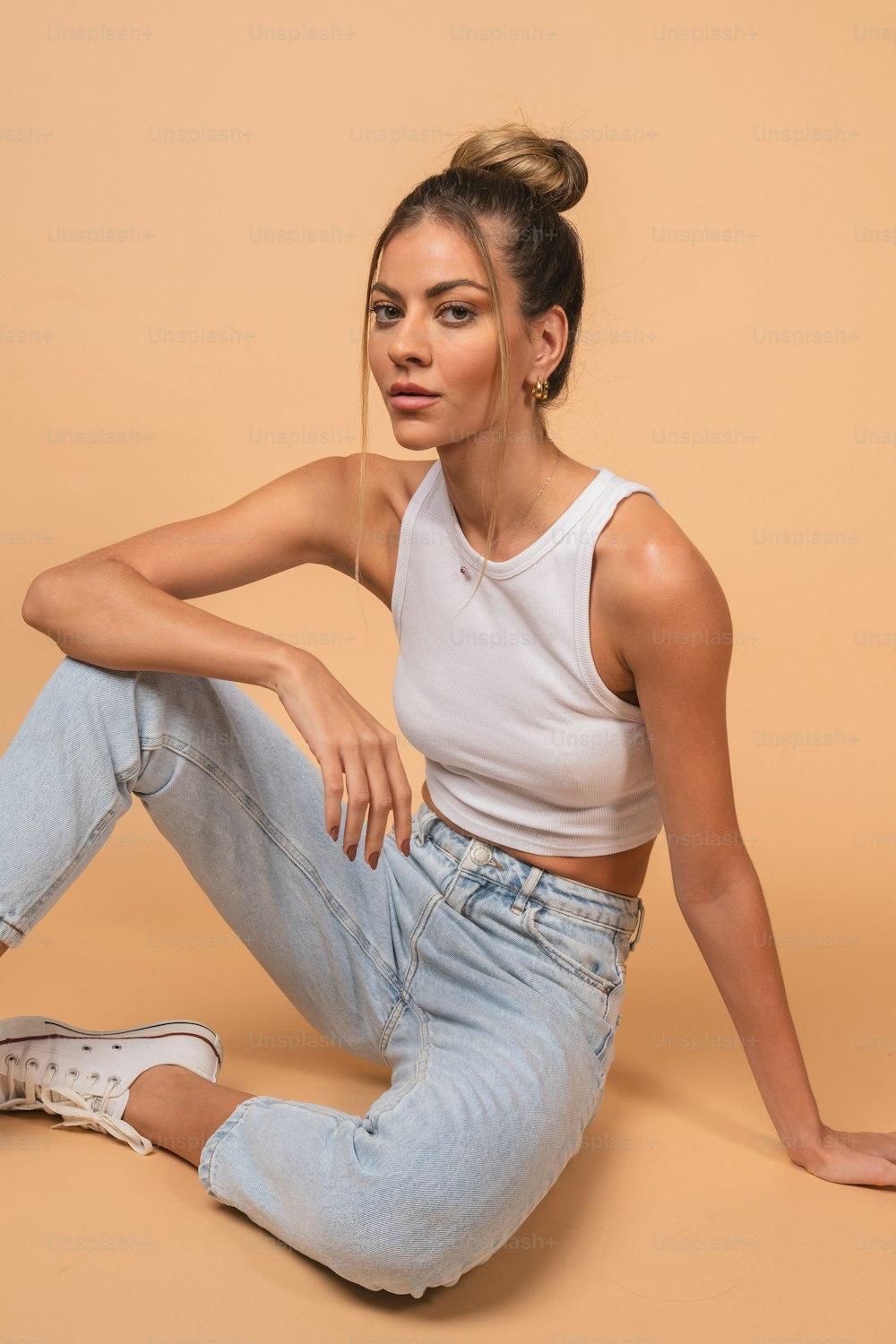 a woman is sitting on the floor wearing jeans and a tank top