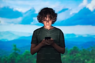 a young boy holding a cell phone in front of a painting
