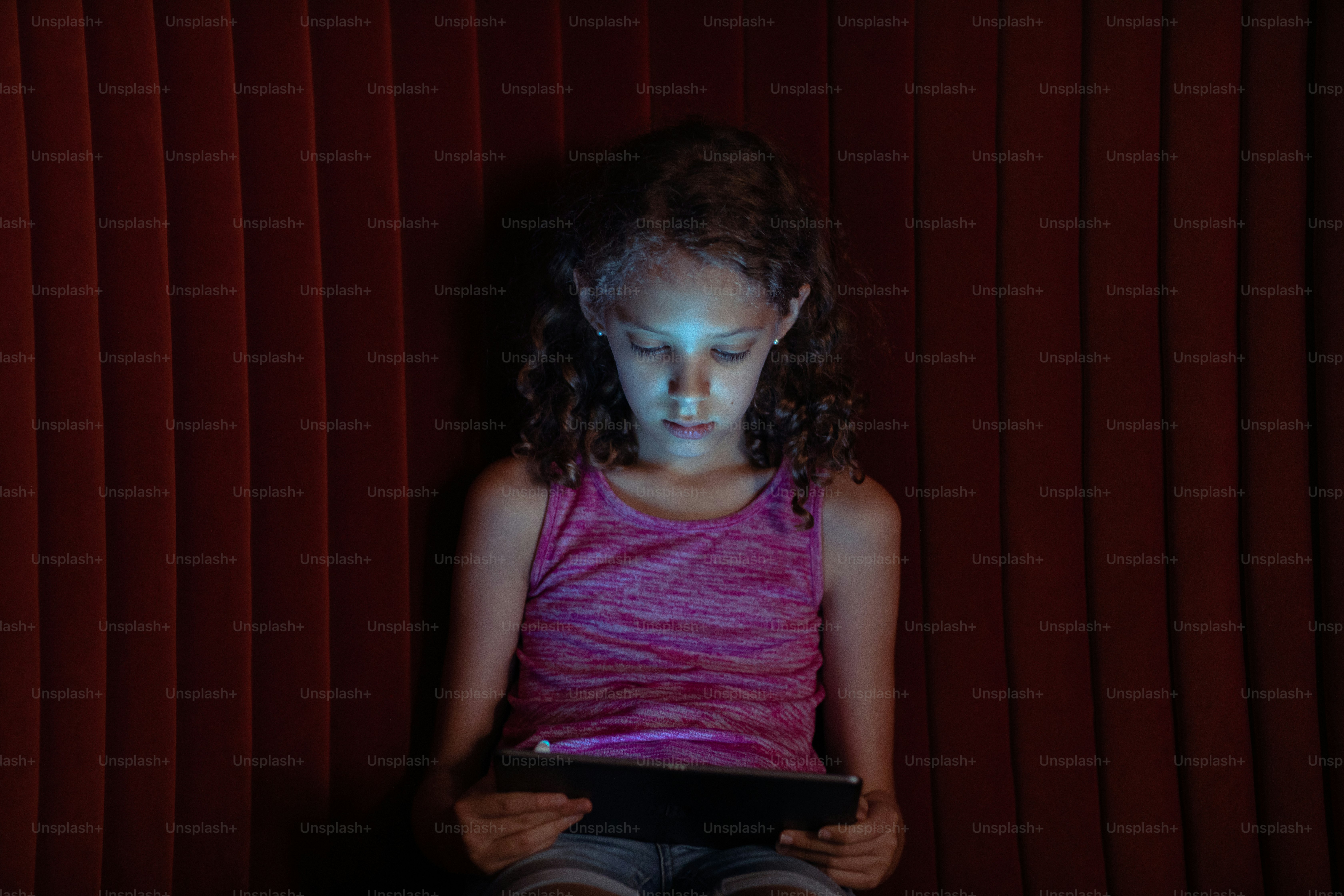 a little girl sitting in front of a red curtain