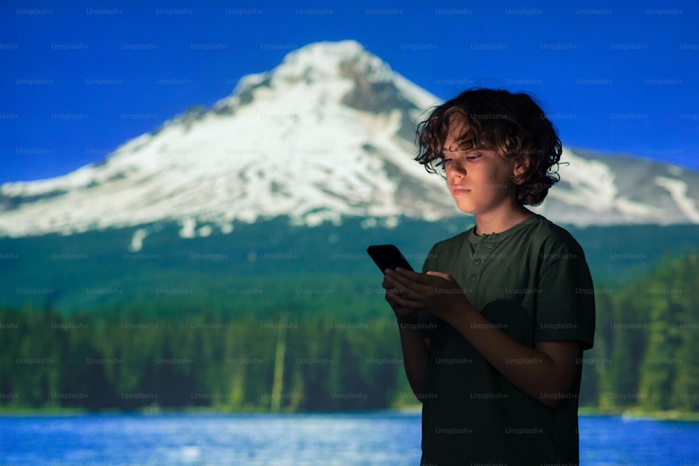 a young boy holding a cell phone in front of a mountain