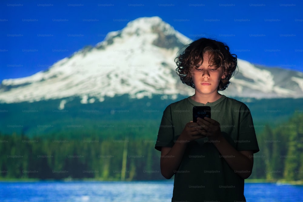 Ein kleiner Junge, der ein Handy vor einem Berg hält