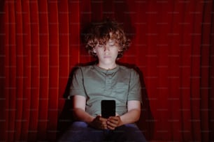 a young boy sitting in a chair holding a cell phone