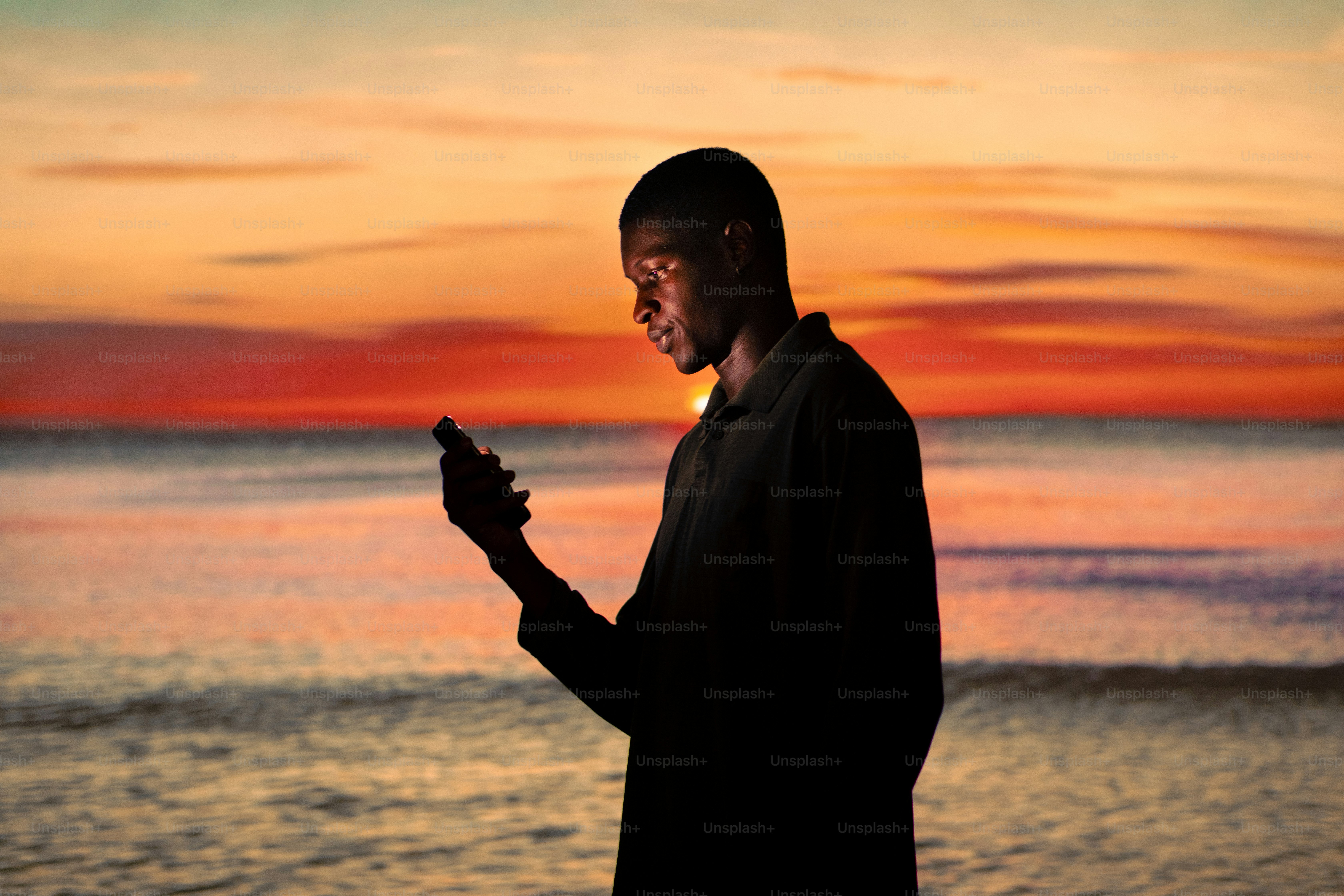 a man standing in front of a sunset holding a cell phone