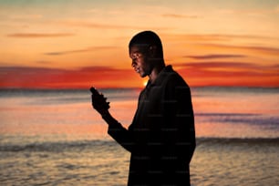 a man standing in front of a sunset holding a cell phone