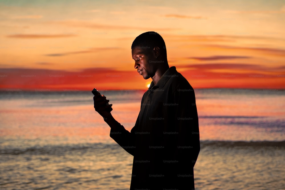 Un hombre parado frente a una puesta de sol sosteniendo un teléfono celular