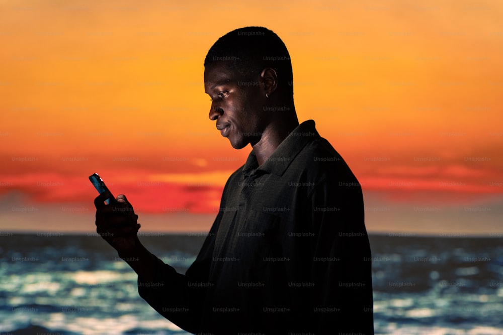 Un hombre parado frente a una puesta de sol usando un teléfono celular