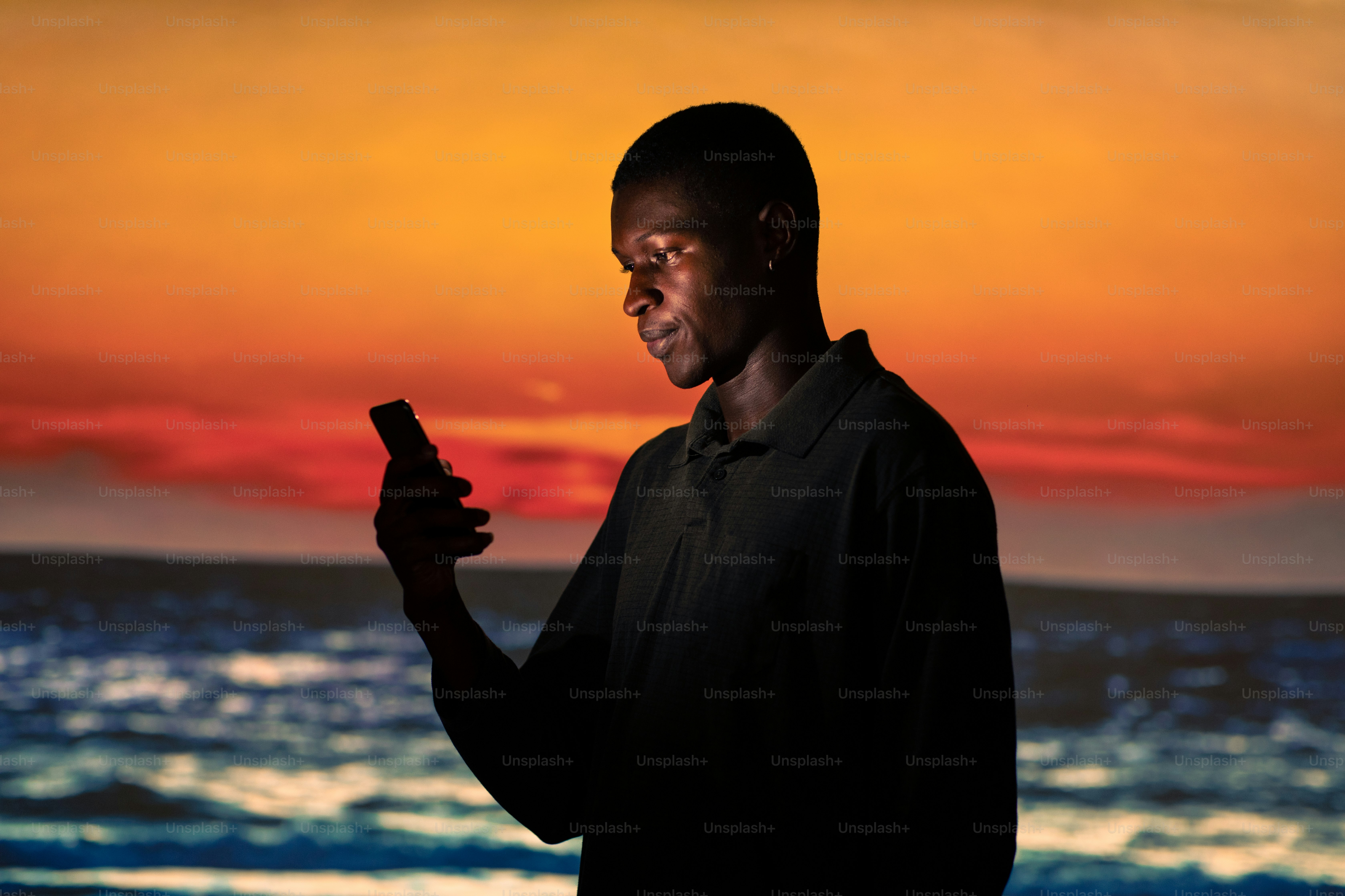 Un hombre parado frente a una puesta de sol sosteniendo un teléfono celular