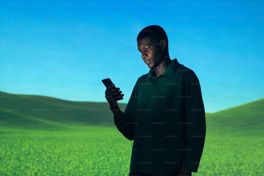 a man standing in a field looking at a cell phone