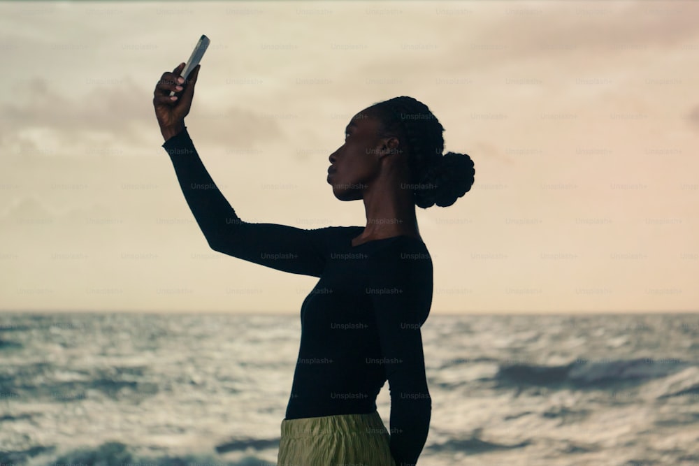 a woman standing on a beach holding a cell phone