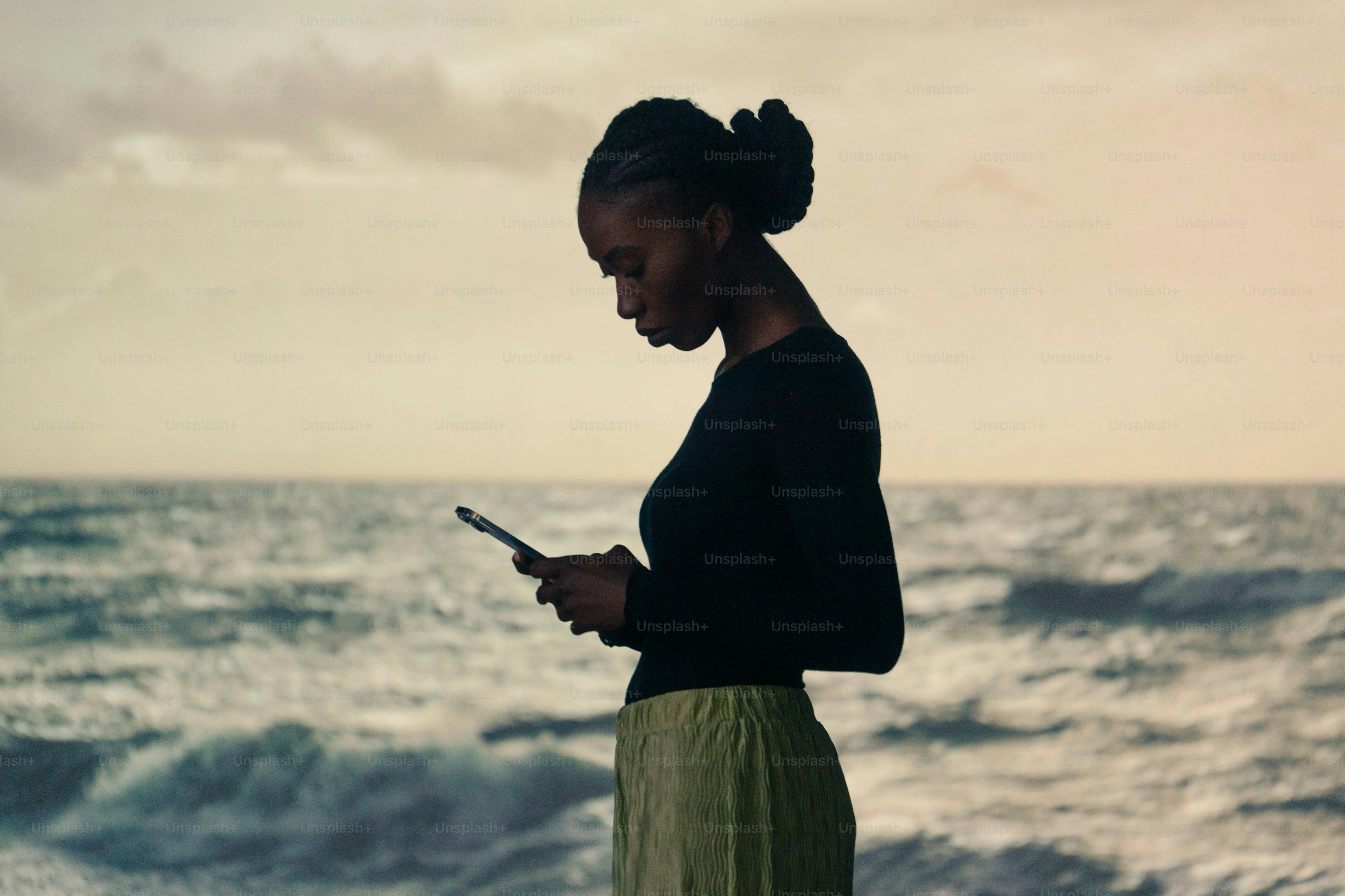 a woman standing on the beach looking at her cell phone