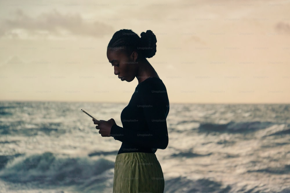 a woman standing on the beach looking at her cell phone