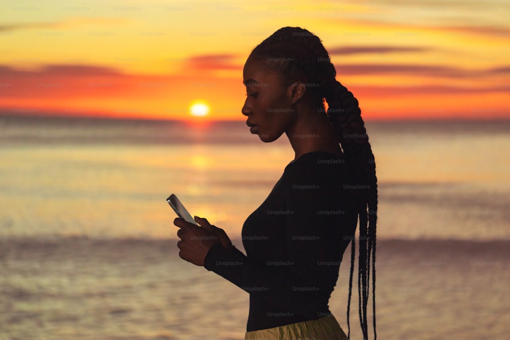a woman standing on a beach looking at her cell phone