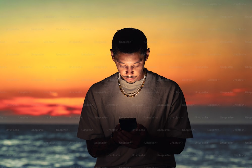 Ein Mann, der mit einem Handy vor einem Sonnenuntergang steht