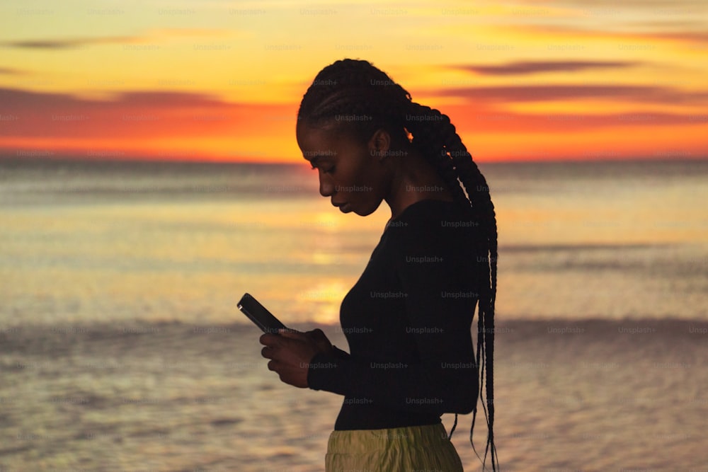 a woman standing on the beach looking at her cell phone