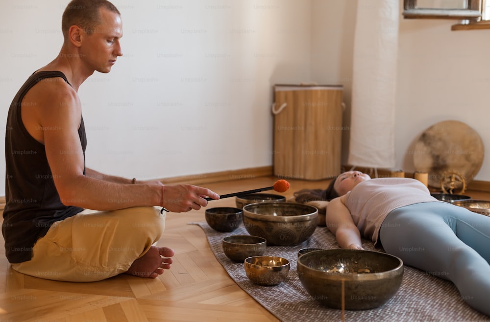 a man and a woman sitting on the floor in front of singing bowls