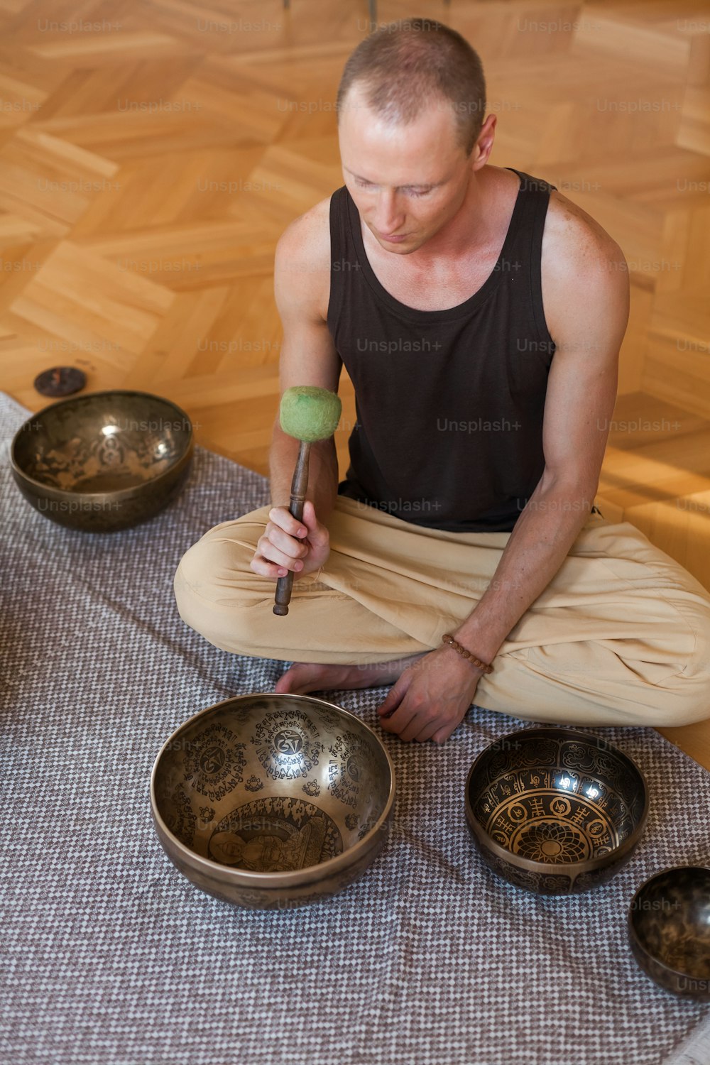 Un homme assis par terre devant un ensemble de bols chantants