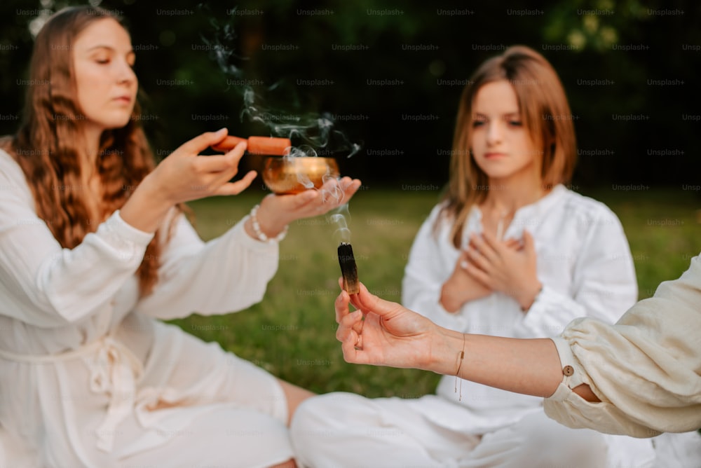 two women sitting on the grass holding a cigarette and a glass of wine