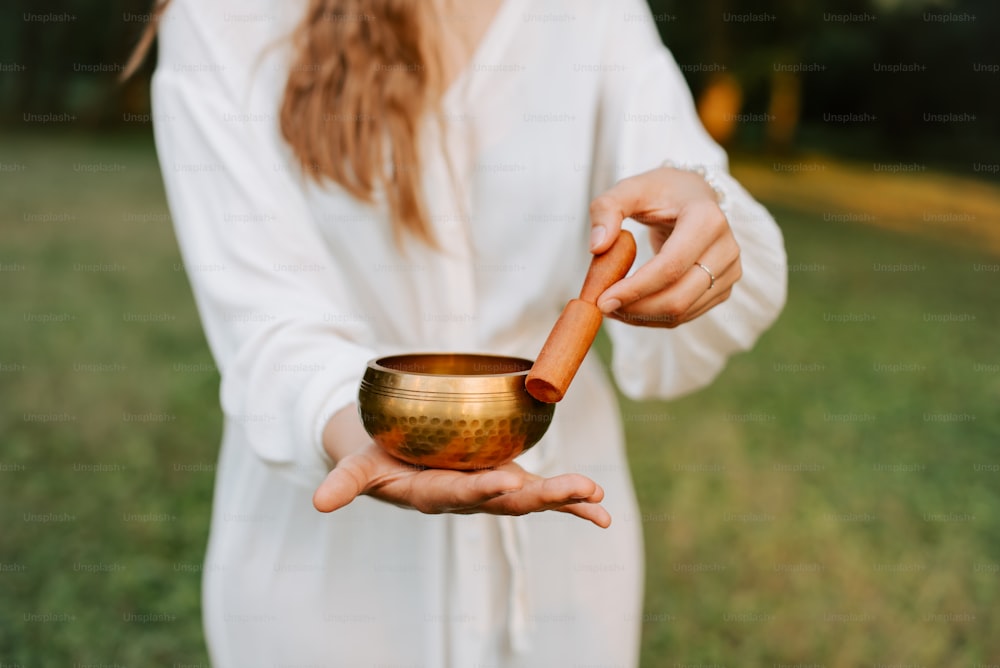 a woman holding a golden singing bowl and a wooden stick