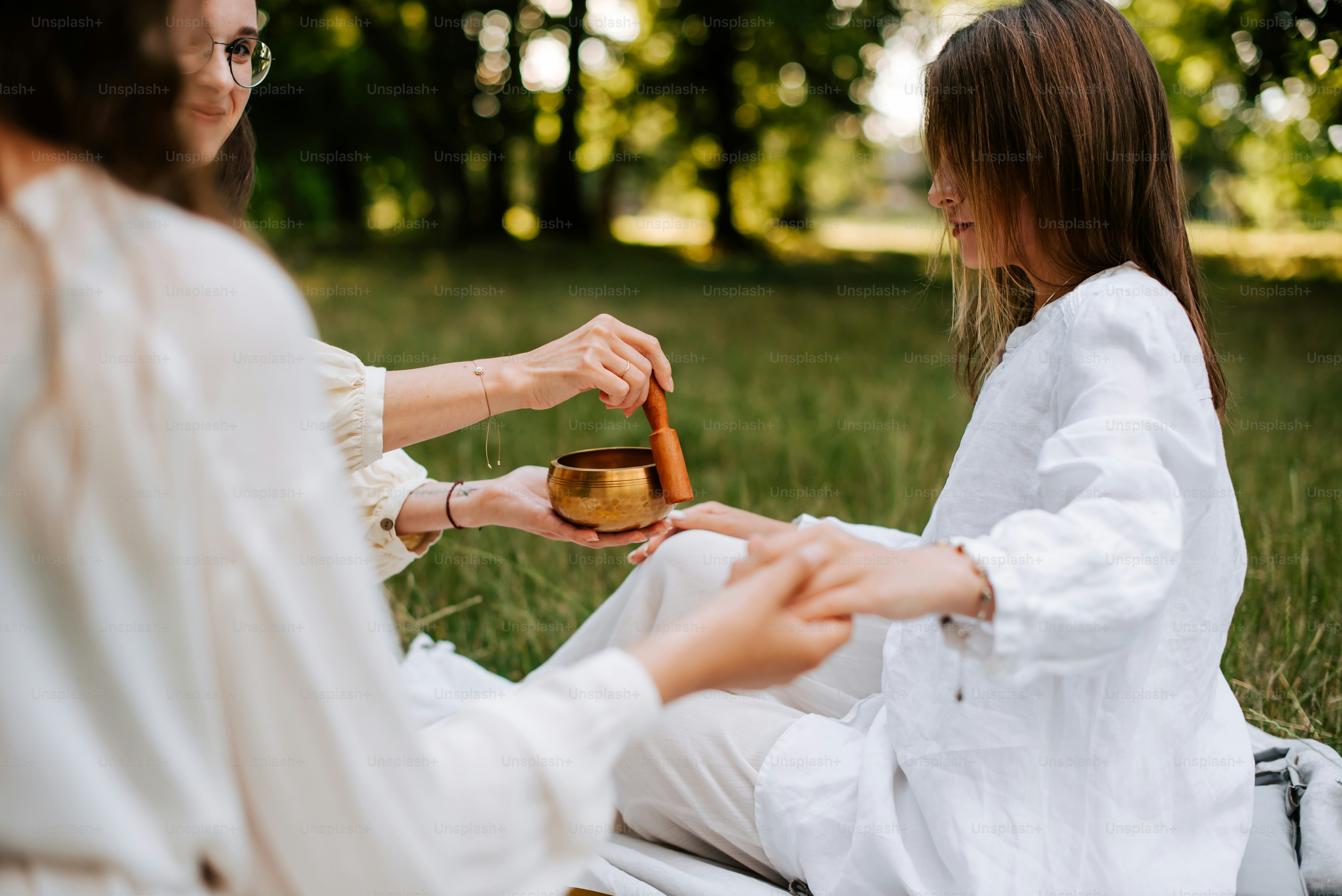 two women sitting in the grass holding a wooden bowl