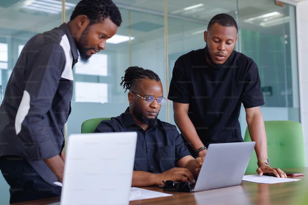 três homens olhando para a tela de um laptop em um escritório