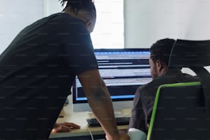 a man standing next to a man sitting in front of a computer