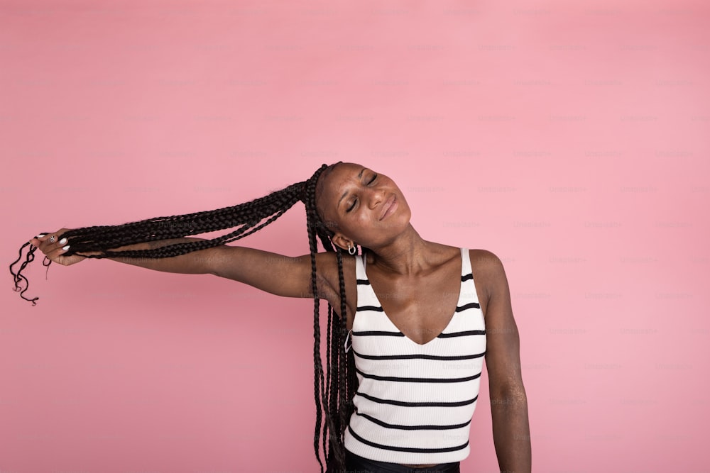 a woman with long braids standing against a pink background