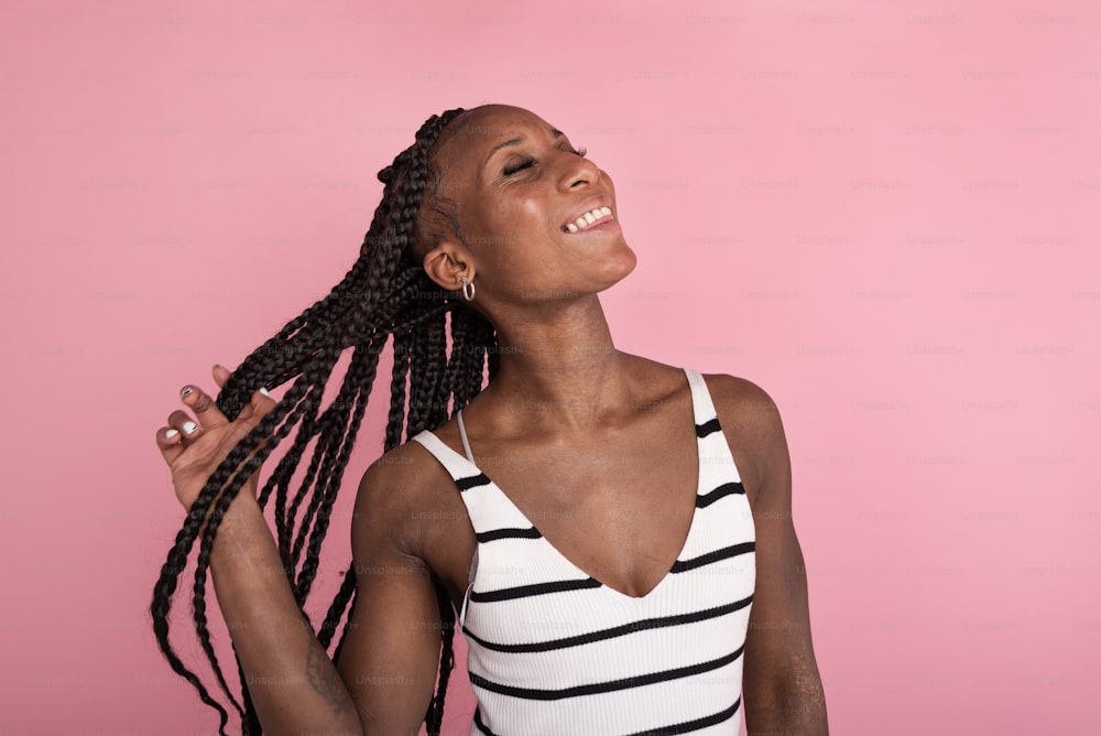 a woman with long braids standing in front of a pink background